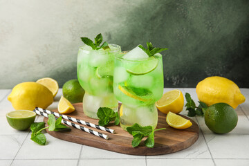 Glasses of delicious cold cocktail and citrus fruits on white tile table, closeup