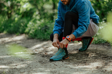 Trail runner tying shoelaces on hiking path in lush forest