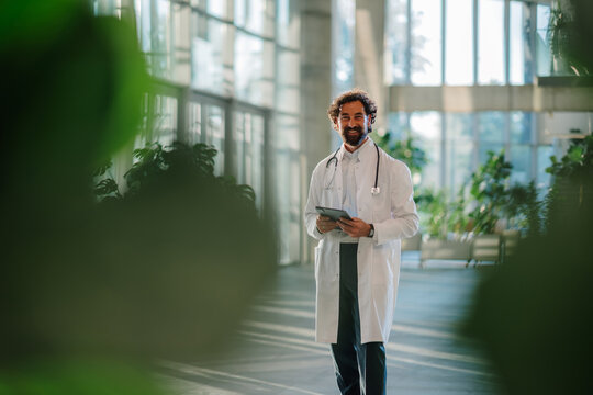Doctor smiling and holding tablet in modern hospital lobby