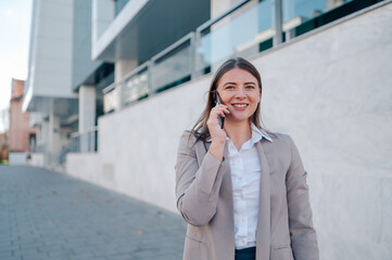 Businesswoman smiling while talking on phone in front of modern office building