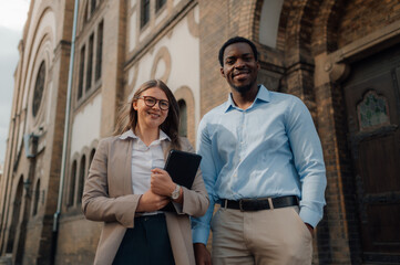 Business people smiling outside institutional building holding tablet