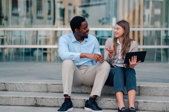 Business colleagues discussing work outdoors with tablet and coffee - Powered by Adobe