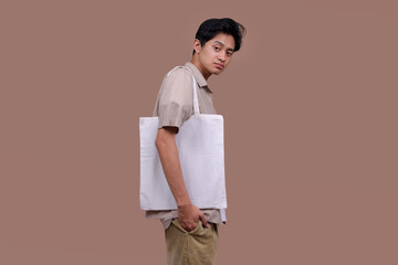 Asian Man Using Reusable White Linen Eco Canvas Tote Bag Against Blank Background for Mockup