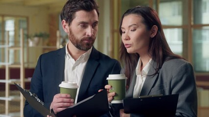 Multiracial two professional business partners holding coffee beverage drink reviewing documents deal Korean woman Caucasian man discussing speaking clipboard paperwork office focused team work report - Powered by Adobe