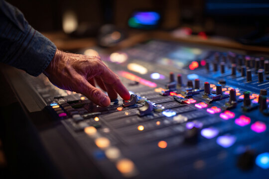 Music producer adjusting audio levels on a sound mixing console in a modern studio at night