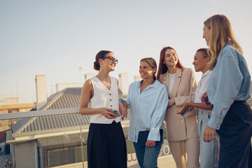 A group of cheerful women is joyfully networking together on a rooftop during a sunny day