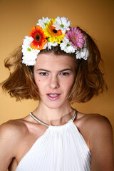 Head shot of fashion model with real flower head decoration on yellow background. Beautiful woman with elegant natural make up and hair, looking at camera, cosmetics concept