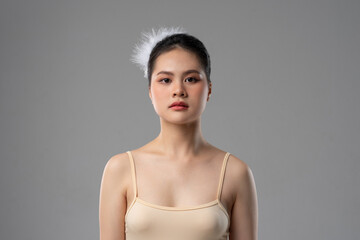 Focused young woman with neutral expression and delicate feather detail in her hair against gray