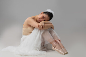 Pensive ballerina embraces knees in studio showcasing elegant ballet attire and serene composure