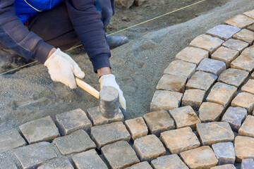 Worker meticulously arranging cobblestones on pathway, demonstrating skilled craftsmanship under...