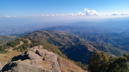 Panoramic vista of rolling hills and distant valley under a clear blue sky, viewed from a rocky outcrop