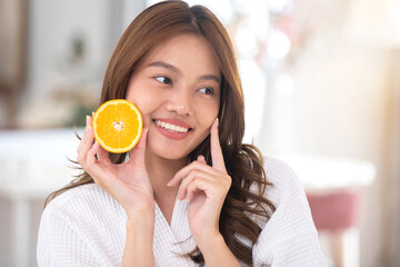 A beautiful Asian woman shows off her regular intake of halved oranges to boost her vitamin C intake. Nourishing your skin with natural