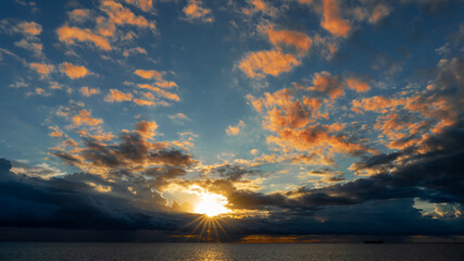 Vibrant fiery sunset over the ocean with silhouettes of cargo ships on the horizon, painting the...