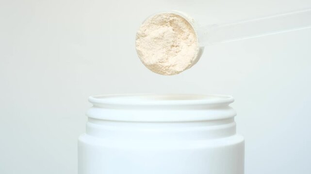 Hand takes protein powder in scoop from plastic jar on gray background close-up.