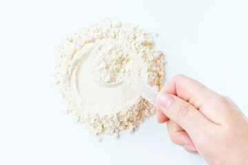Female hand putting plastic scoop on scattered protein powder on white background.