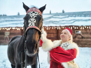 Beautiful Russian girl in national dress poses with horse during Maslenitsa celebration in winter