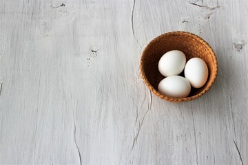 White eggs in a wicker basket on a white wooden background