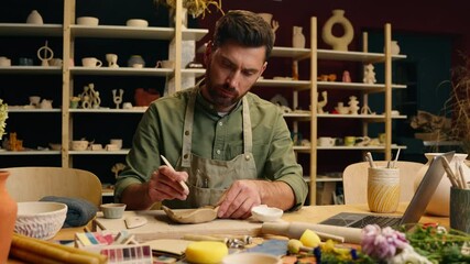 Caucasian man male small business creating artist craftsman potter practicing listening tutorial online video call laptop web computer nodding head creating sculpt crockery pottery artwork at workshop - Powered by Adobe