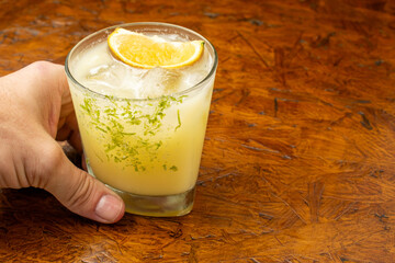 Hand holding a classic citrus Margarita or Caipirinha cocktail with a lime zest rim and fresh...