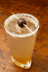 Exotic Tamarind (Tamarindo) Margarita cocktail with a salt and chili rim, garnished with fresh tamarind fruit; a traditional Latin American summer drink served on a wooden bar table.