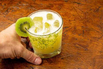 Hand holding a refreshing Kiwi Margarita cocktail with lime zest rim and fresh kiwi slice garnish,...