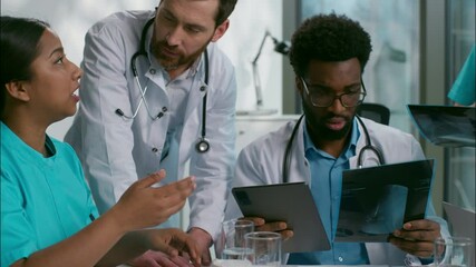 Close up professional multiethnic diverse team of experienced doctors men women five medical people talking brainstorming diagnosis using laptop device tablet analyzing scan difficult case at hospital - Powered by Adobe