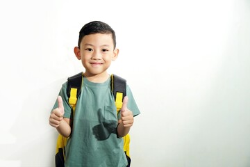 Confident boy giving thumbs up with both hands while smiling. Wearing backpack and standing against white background.