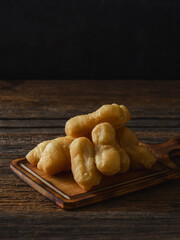 Golden Fried Dough Sticks on Wooden Platter Against Dark Background
