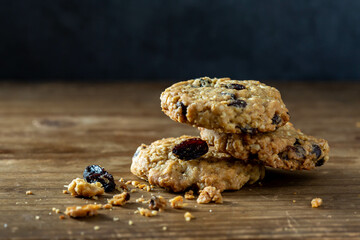 Oatmeal raisin cookies stacked on wooden surface with crumbs
