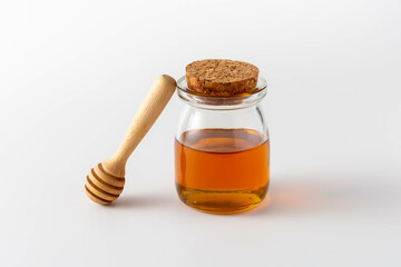 Glass Jar of Honey with Wooden Dipper and Cork Lid on White Background