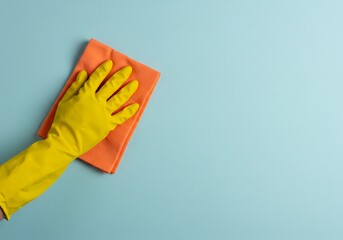 A worker wearing a yellow rubber glove dusts a pastel blue wall with a blue cloth &mdash; representing general or routine cleaning by a commercial cleaning service.