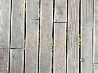 Close-up of weathered wooden planks with small green grass sprouting between the gaps. Natural texture and outdoor flooring detail.