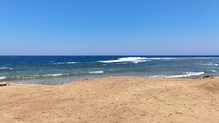 A sandy beach along the Red Sea coast in Egypt. Small waves roll onto the shore. Clear blue sky, sunny day, background for summer holidays and tourism