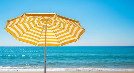 Yellow and white striped beach umbrella on a sandy beach with blue ocean view