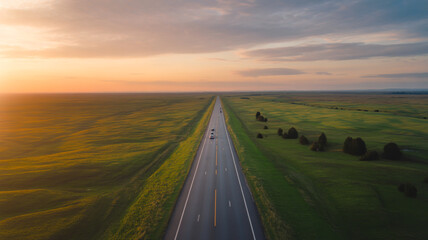 A long, straight road stretching through green fields towards the horizon at sunset, symbolizing a journey