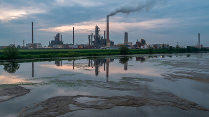 An industrial landscape showing factory pollution reflected in water, highlighting the environmental impact of industry