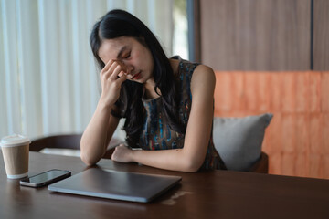 Stressed young asian businesswoman having headache while working on laptop in cafe