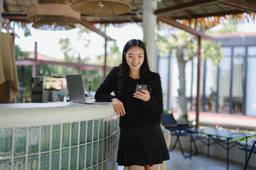 Obraz premium Young Asian businesswoman using smartphone and laptop in outdoor cafe