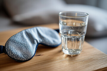 flat lay of glass of water and sleep mask on wooden bedside table, summer evening atmosphere, 