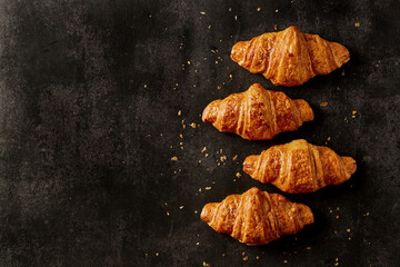 French croissants with crumbs on a dark background. Top view, horizontal orientation, selective...