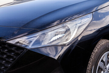 The headlight of a car is lit up. The car is blue. The sky is cloudy