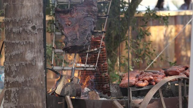 Traditional Argentine barbecue with sausages and beef cuts cooking on open fire grill at rustic outdoor setting.