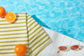 Fresh tangerines and striped towel add vibrant color to a white tiled poolside scene. The direct...