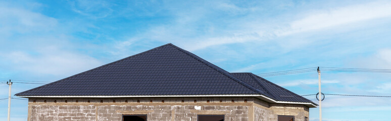 A house with a metal slate roof and a white wall. The roof is sloping and the house is made of brick.