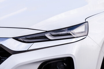 The headlight of a white car is lit up. The light is on the front of the car
