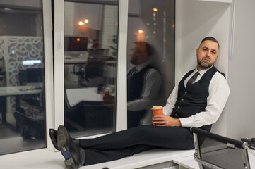 Thoughtful Caucasian man sitting on windowsill in office. 