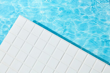 Bright sunlight reflects off clear pool water and smooth white mosaic tiles, forming a clean...