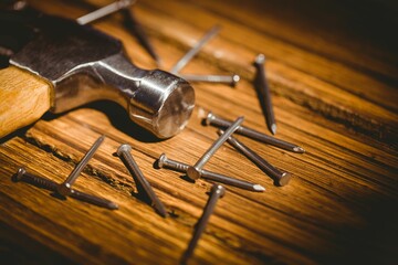 Flat design showing metallic hammer head with wooden handle resting on plank, featuring steel nails