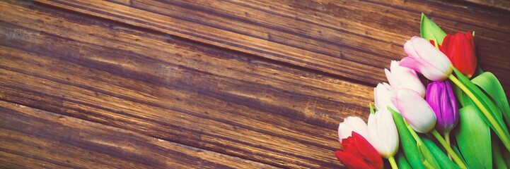 Bouquet of multicolored tulips is resting on wooden tabletop in flat design, showing grain texture