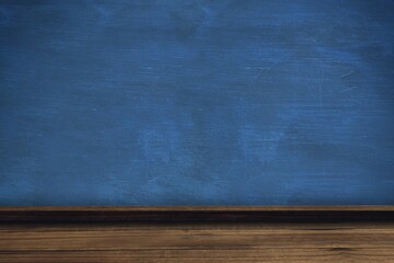 Blue chalkboard is sitting above wooden ledge and desk in classroom showing chalk smudges